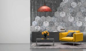 grey room with a hexagon designed wall, long dark grey dresser against the wall with brown and white book on top, yellow armchair with grey pillows, coffee table with yellow flowers, a red and brown ceiling light